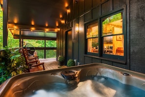 Un espace avec un jacuzzi, une terrasse en bois, une chaise et une vue sur la cuisine à travers une fenêtre.