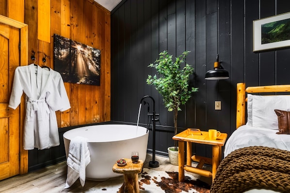 Une pièce avec une grande baignoire, des murs en bois, un lit en bois, une petite table avec une tasse et un bol, et une plante.