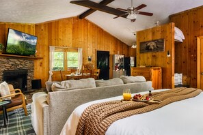 Une chambre confortable dans un chalet en rondins, avec une cheminée en pierre, un grand lit, un canapé et un coin repas.
