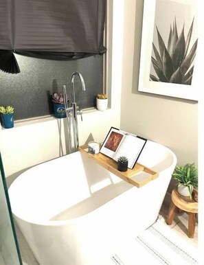 Bathroom features a bathtub, framed picture, and a small potted plant.