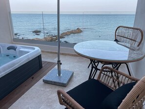 Un balcón con hidromasaje, sillones de mimbre y una mesa con cubierta de vidrio con vista al mar.