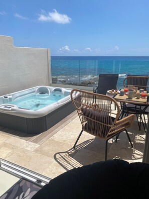 Un jacuzzi y sillones de mimbre en un balcón con vista al océano.