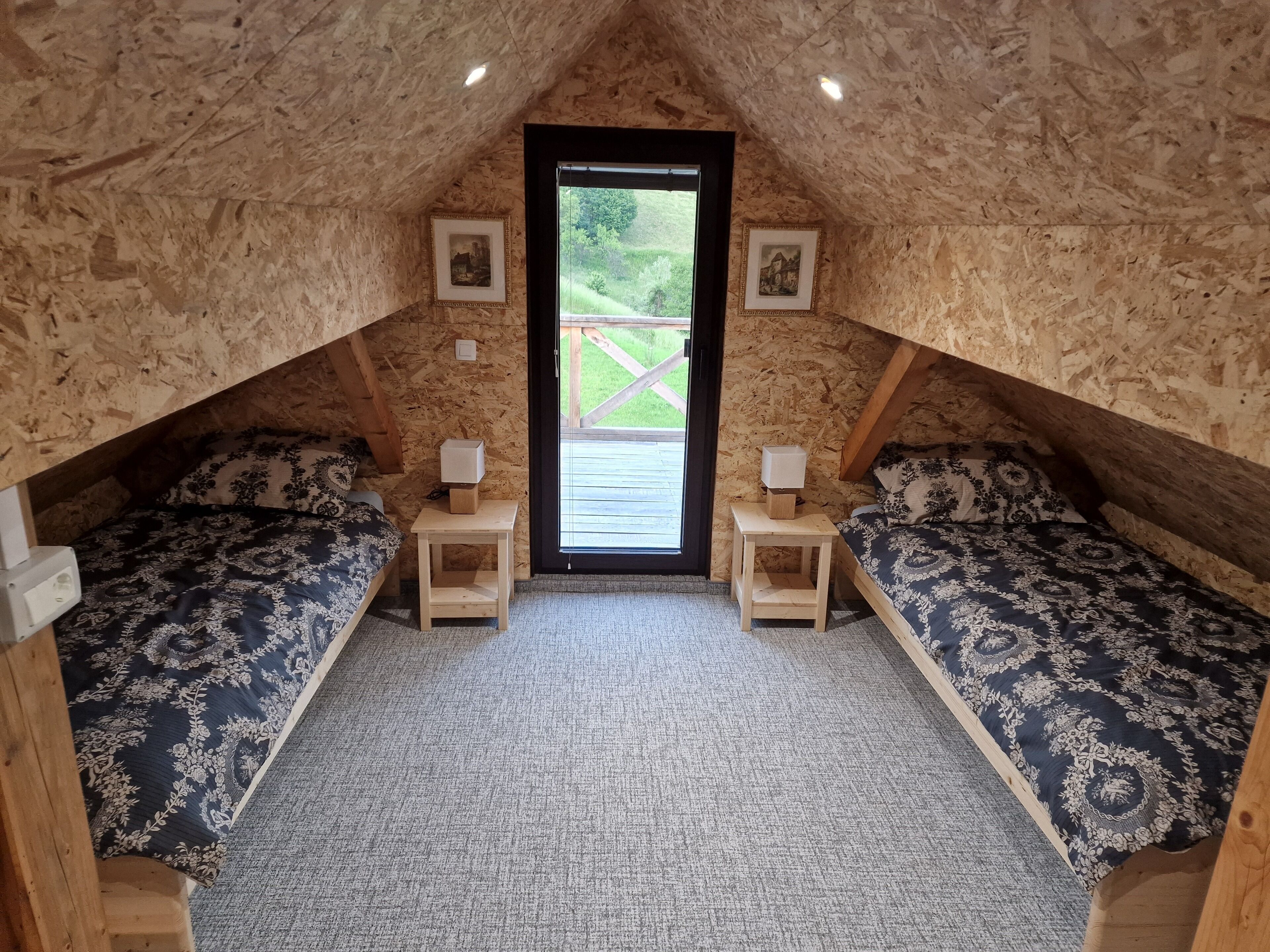 Ein gemütliches Schlafzimmer im Dachgeschoss mit zwei Betten, jeweils mit passendem Kopfteil und Fußteil, einem kleinen Nachttisch mit Lampe und gerahmten Bildern an den Wänden.