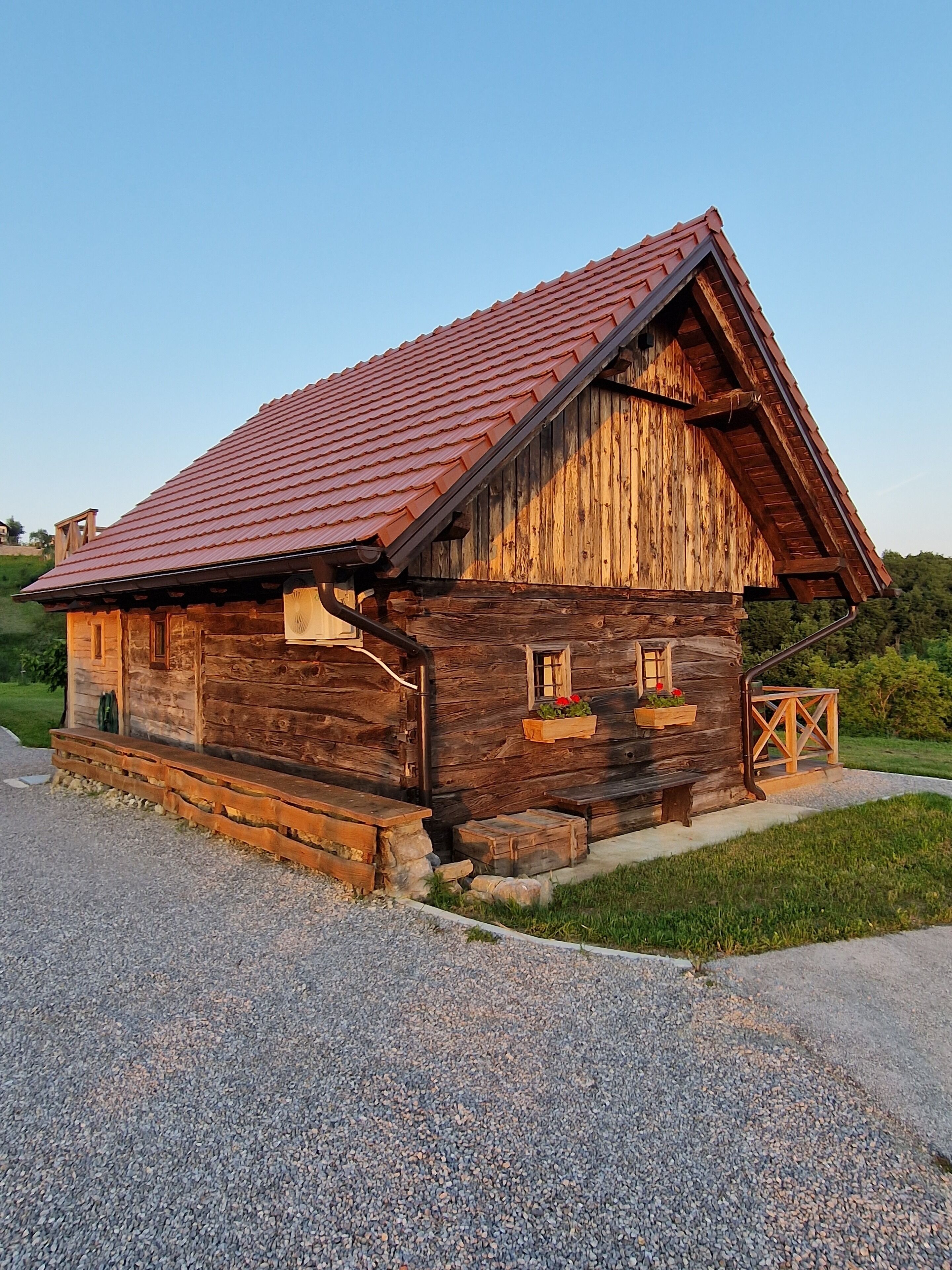 A rustic wooden cabin with a sloped red roof, a wooden porch, and a small window with a flower box.