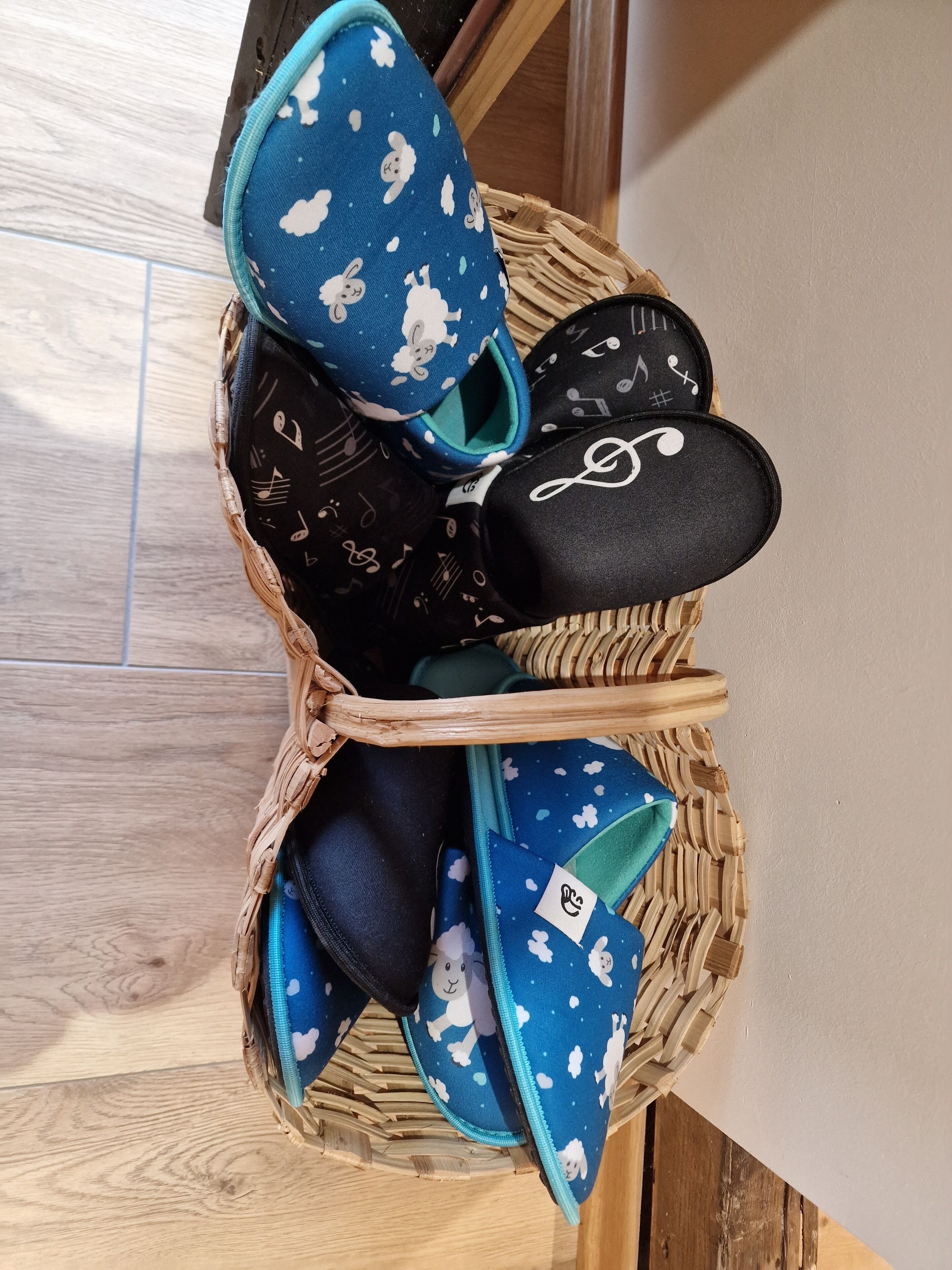 A wicker basket containing various slippers with different patterns and designs.