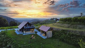 Eine rustikale Holzhütte mit Veranda und einem kleinen Schuppen, umgeben von üppigem Grün und Hügeln.