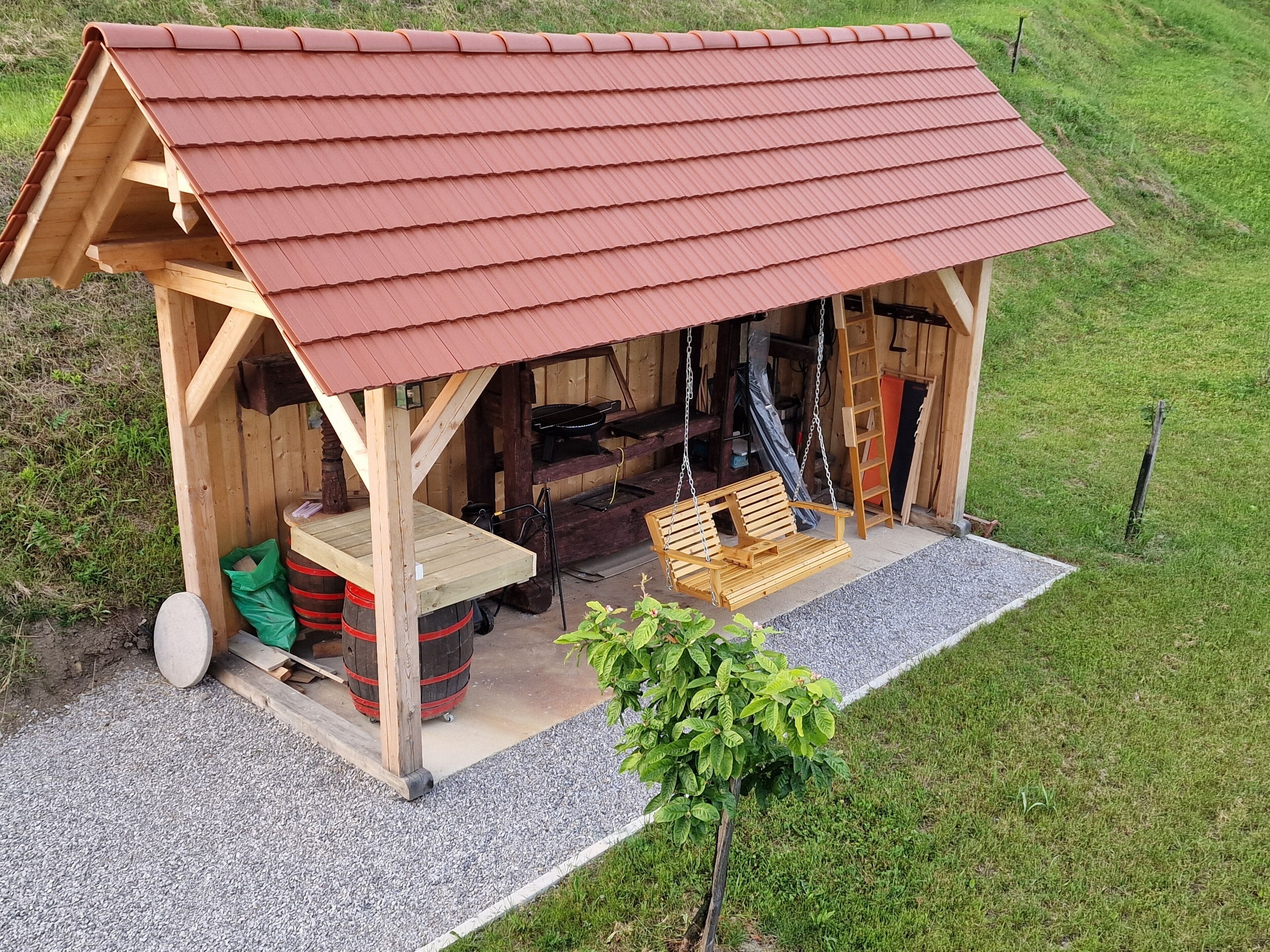 A wooden structure with a red roof, a swing seat, and a small table.