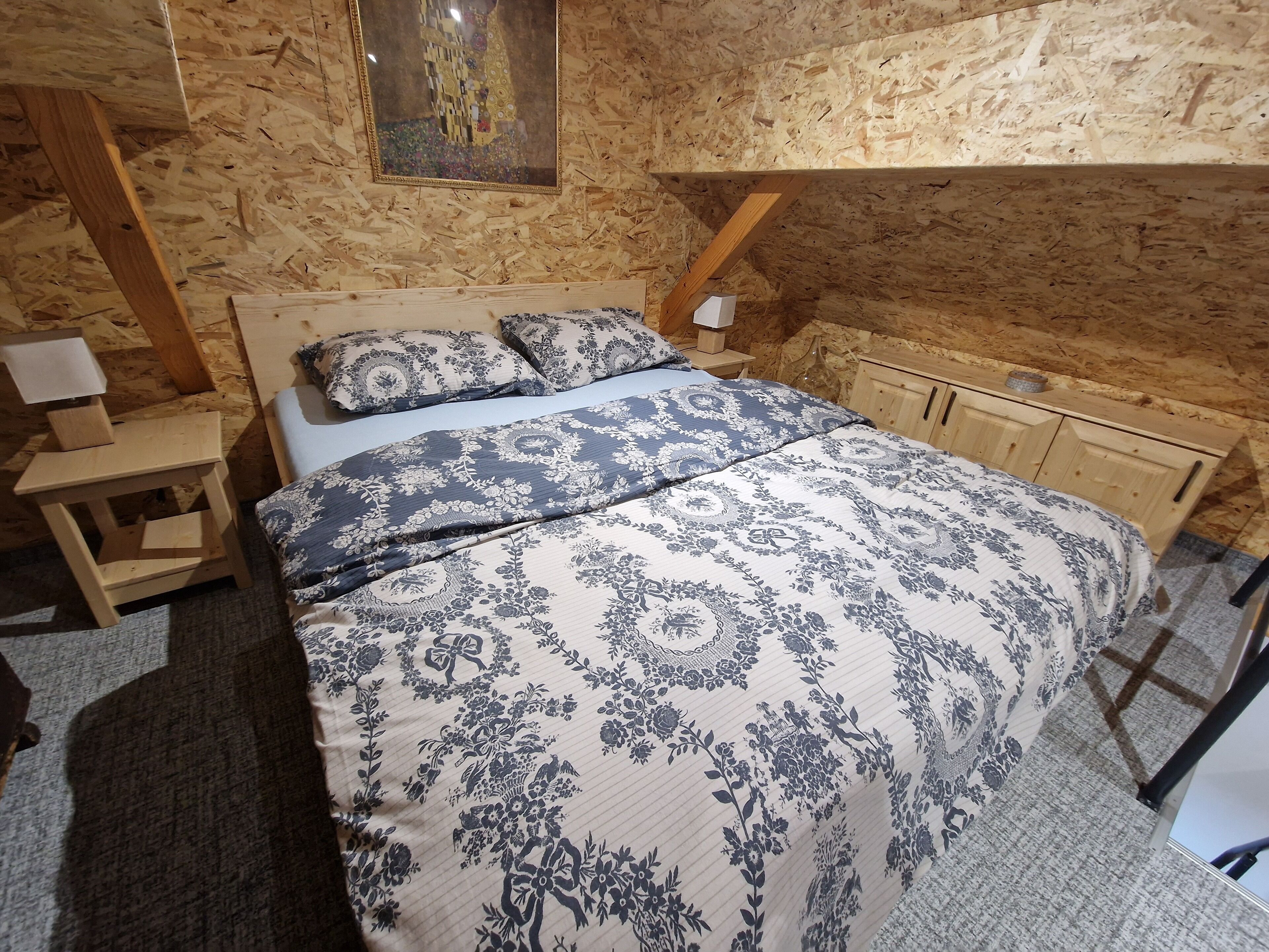 Een slaapkamer met een houten plafond, een bed met bloemenbeddengoed, een nachtkastje en een houten kast.