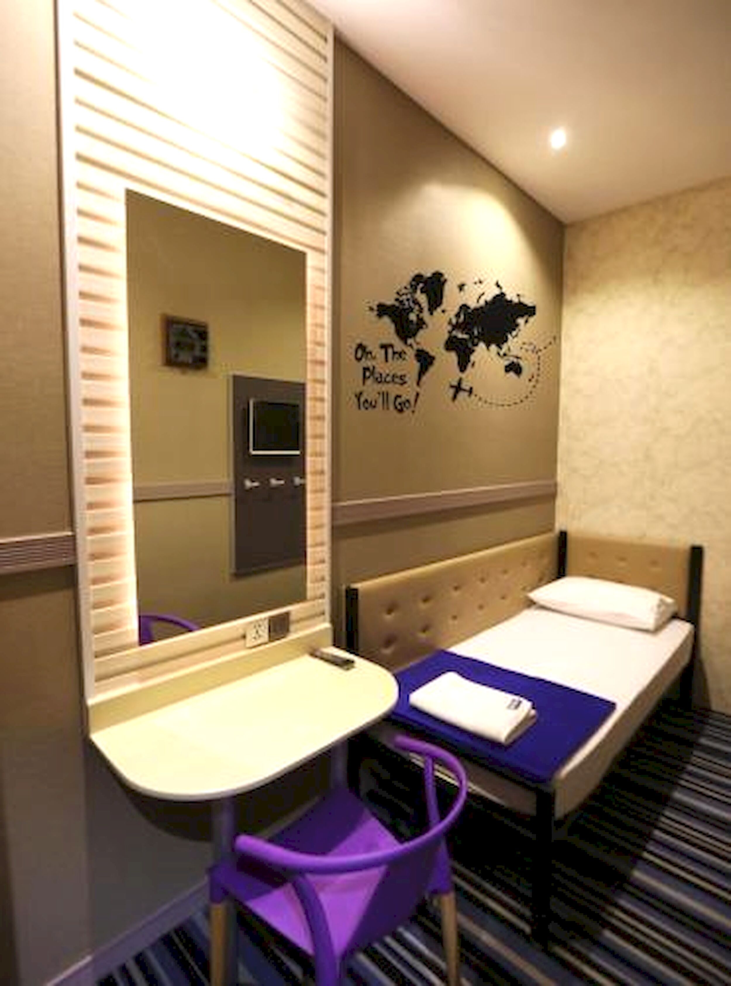 A hotel room with a bed, a desk with a chair, a mirror, and a world map on the wall.