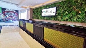 A reception area with a green wall and a sign that reads "PodSteL Hostel Bangkok".