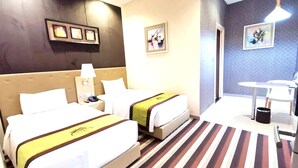A hotel room with two beds, a small desk, a chair, and a trash bin.