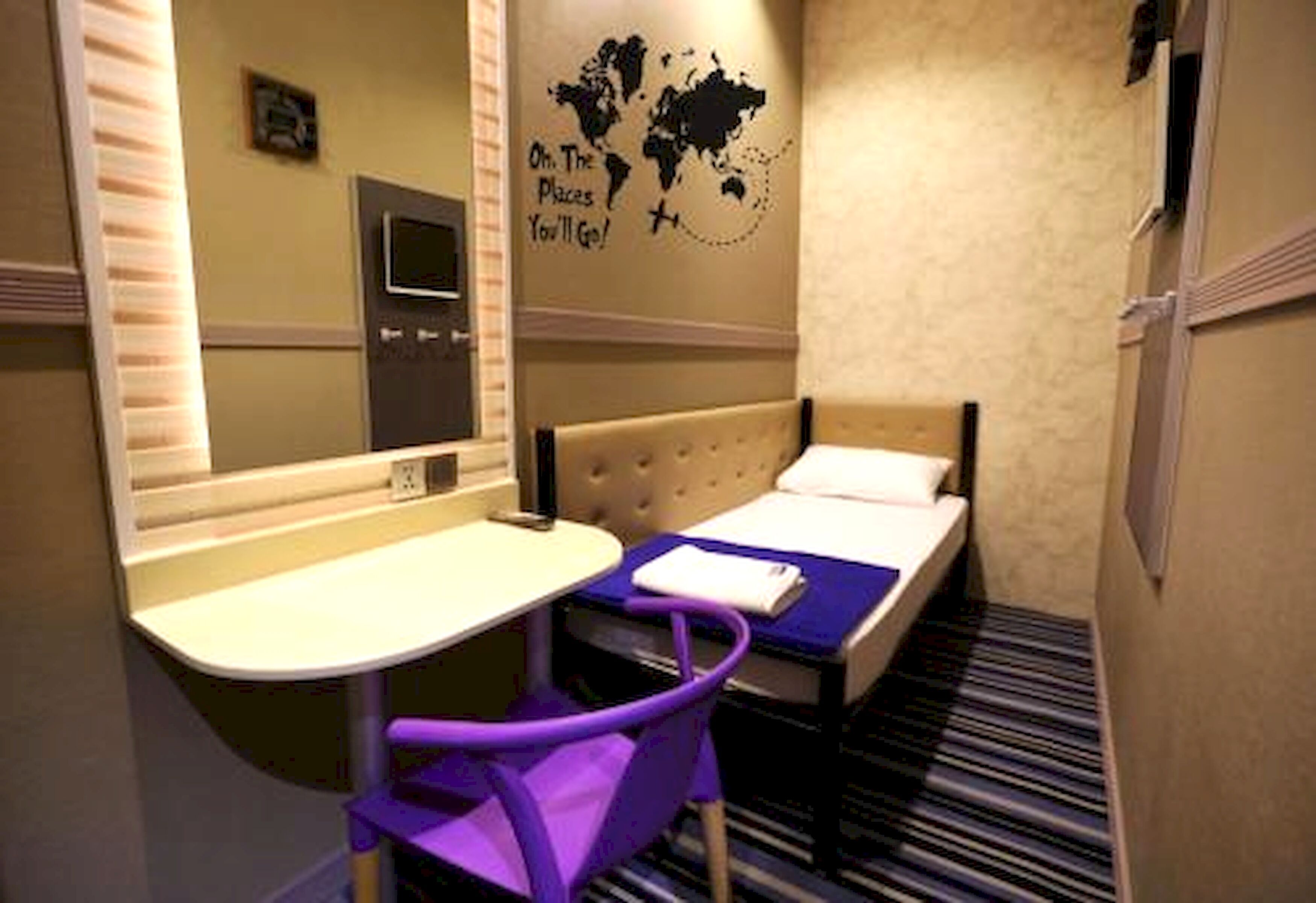 A hotel room with a bed, a desk with a chair, a mirror, and a world map on the wall.