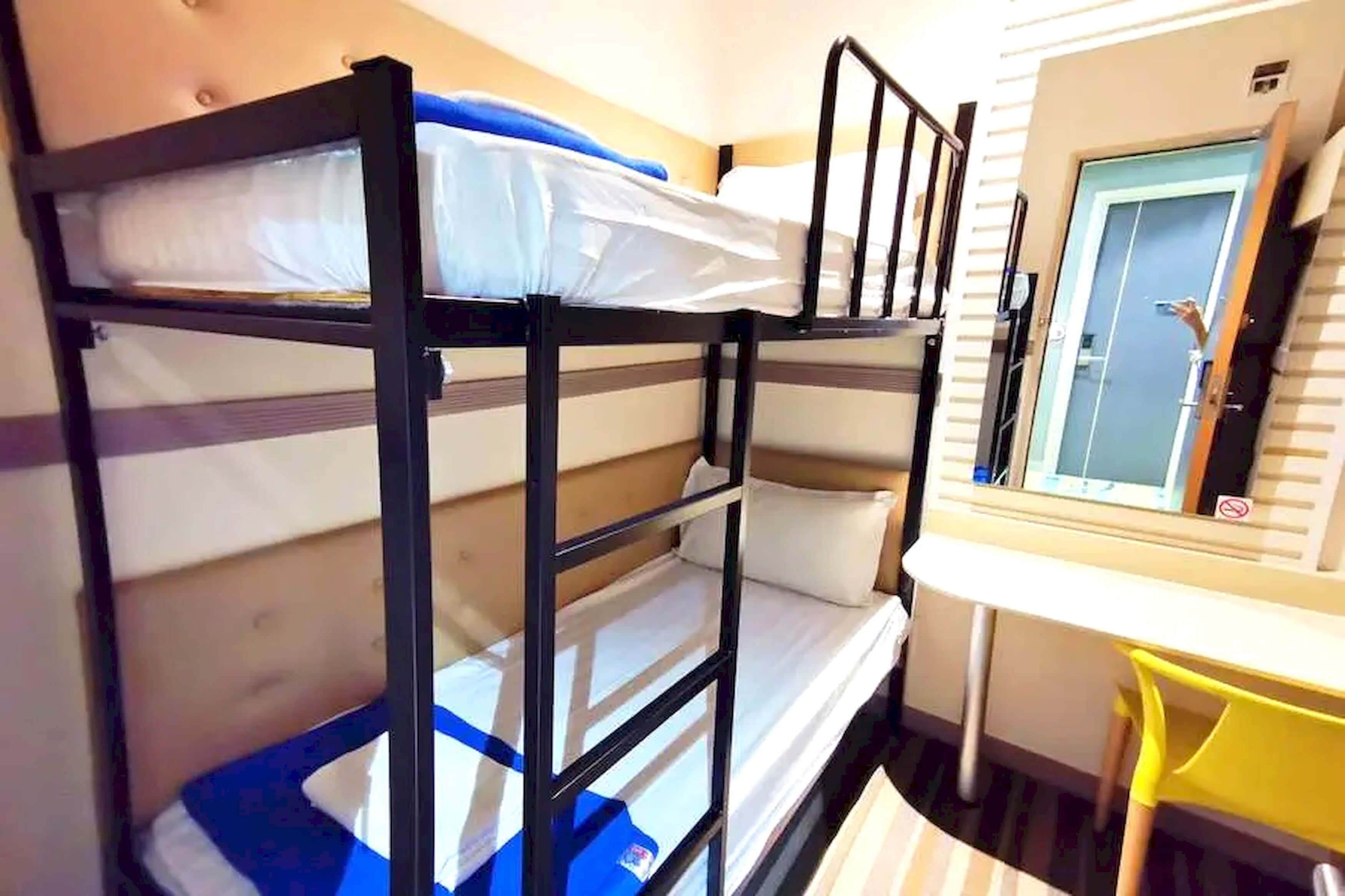 A bunk bed room with a desk and chair, a door, and a window.