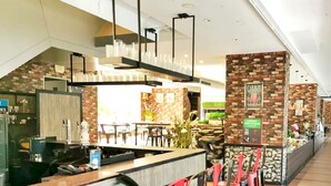A modern restaurant with a long counter, red chairs, and a brick wall.