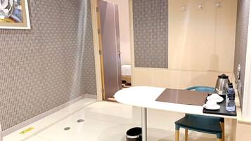A hotel room with a bed, a table with a chair, a coffee maker, and a trash bin.
