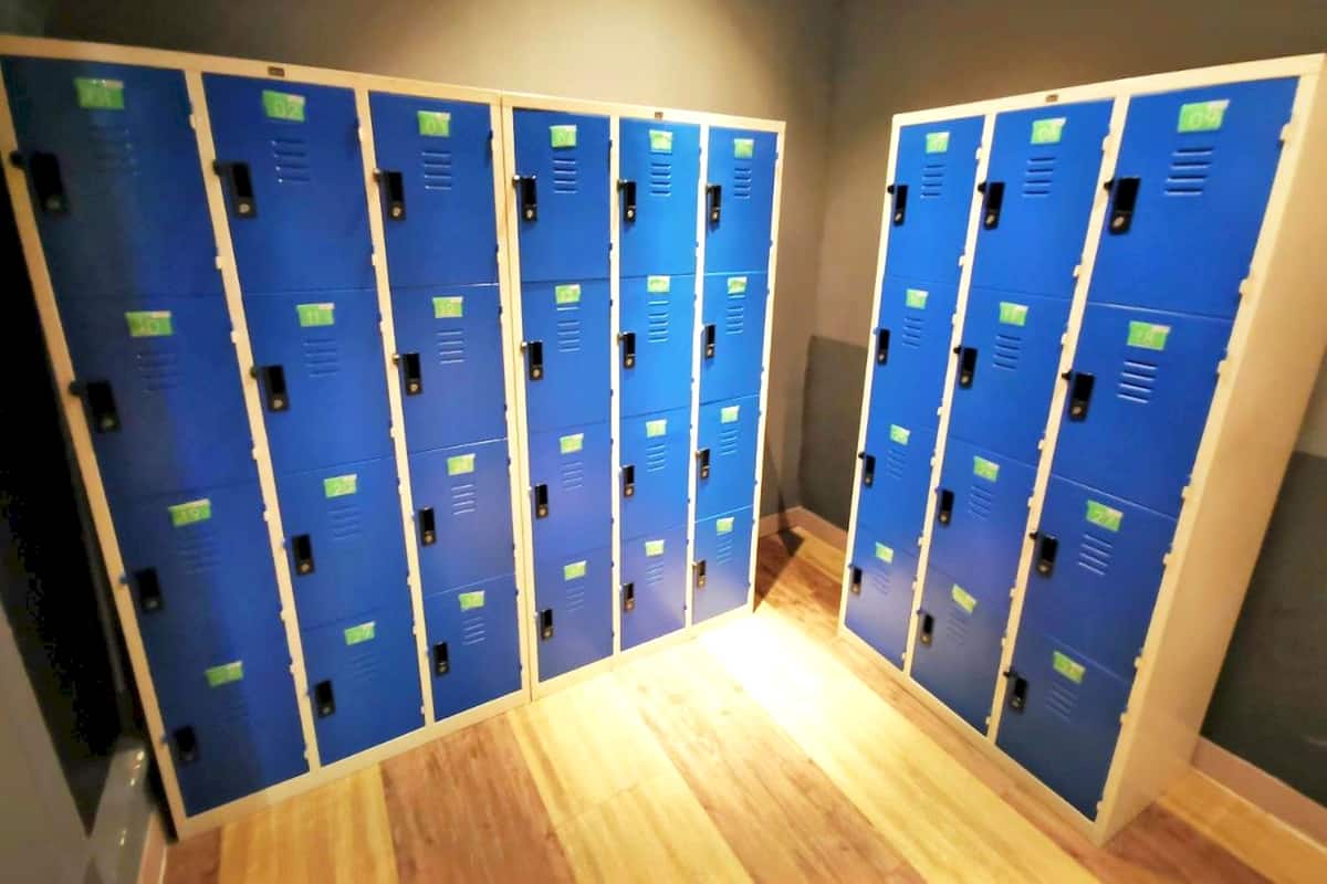 Une rangée de casiers bleus avec des étiquettes vertes, un plancher en bois et un mur gris.