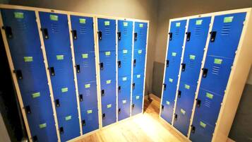 A row of blue lockers with green labels, wooden flooring, and a grey wall.