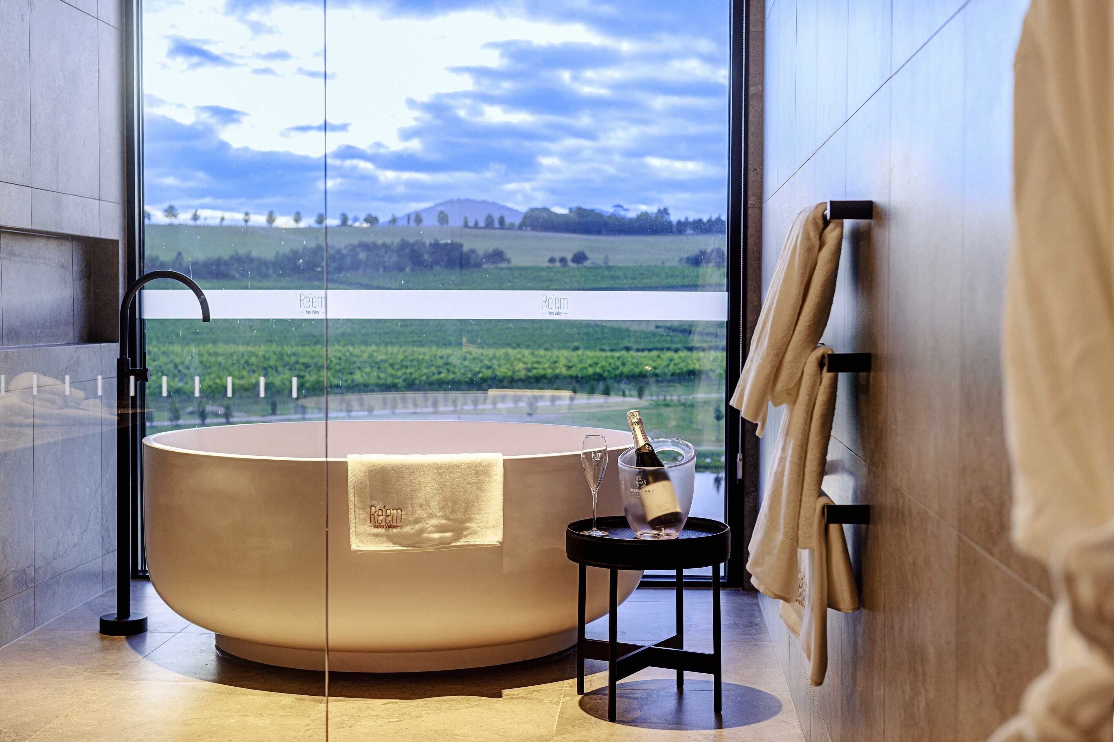A modern bathroom with a large bathtub, a glass-enclosed shower, and a view of a green landscape.