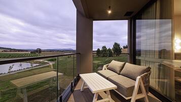 A balcony with a sofa and table, overlooking a vineyard and a body of water.