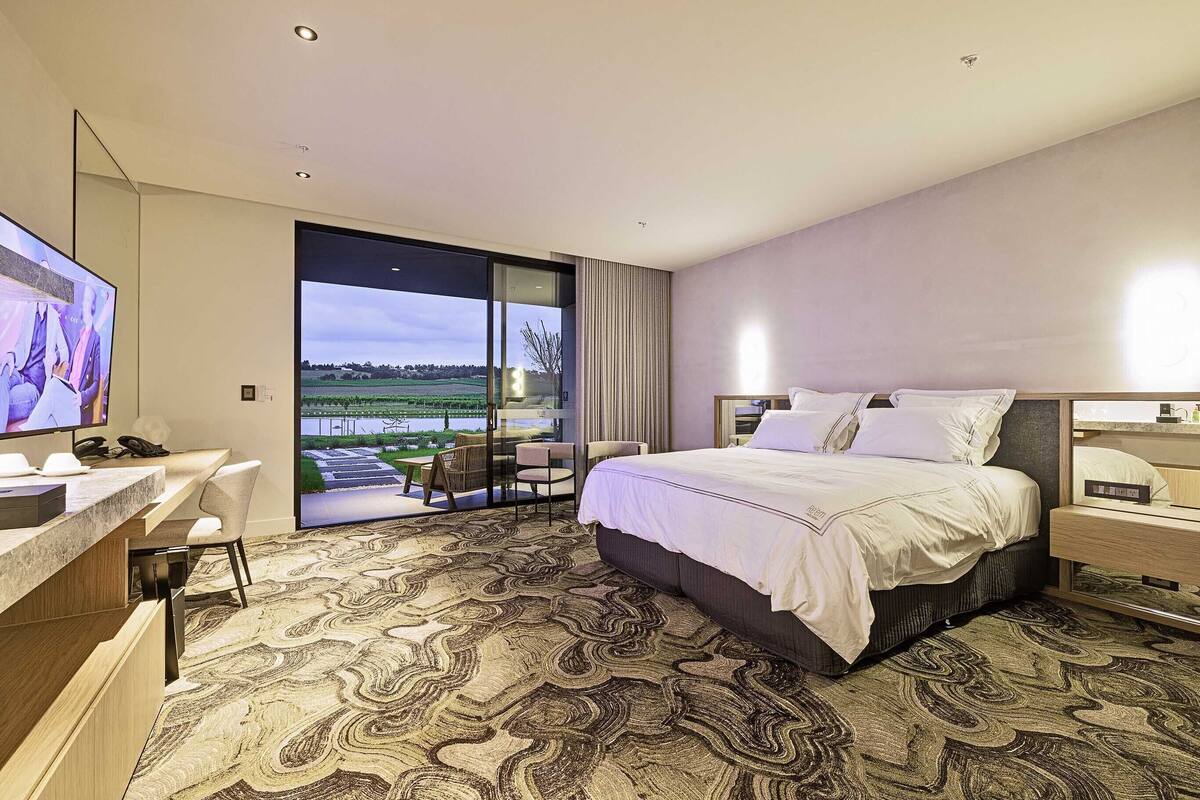 Habitación de hotel moderna con una cama grande, un escritorio y un balcón con vistas a un paisaje verde.