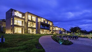Un edificio moderno de varios pisos con amplias ventanas y un exterior bien iluminado al anochecer.