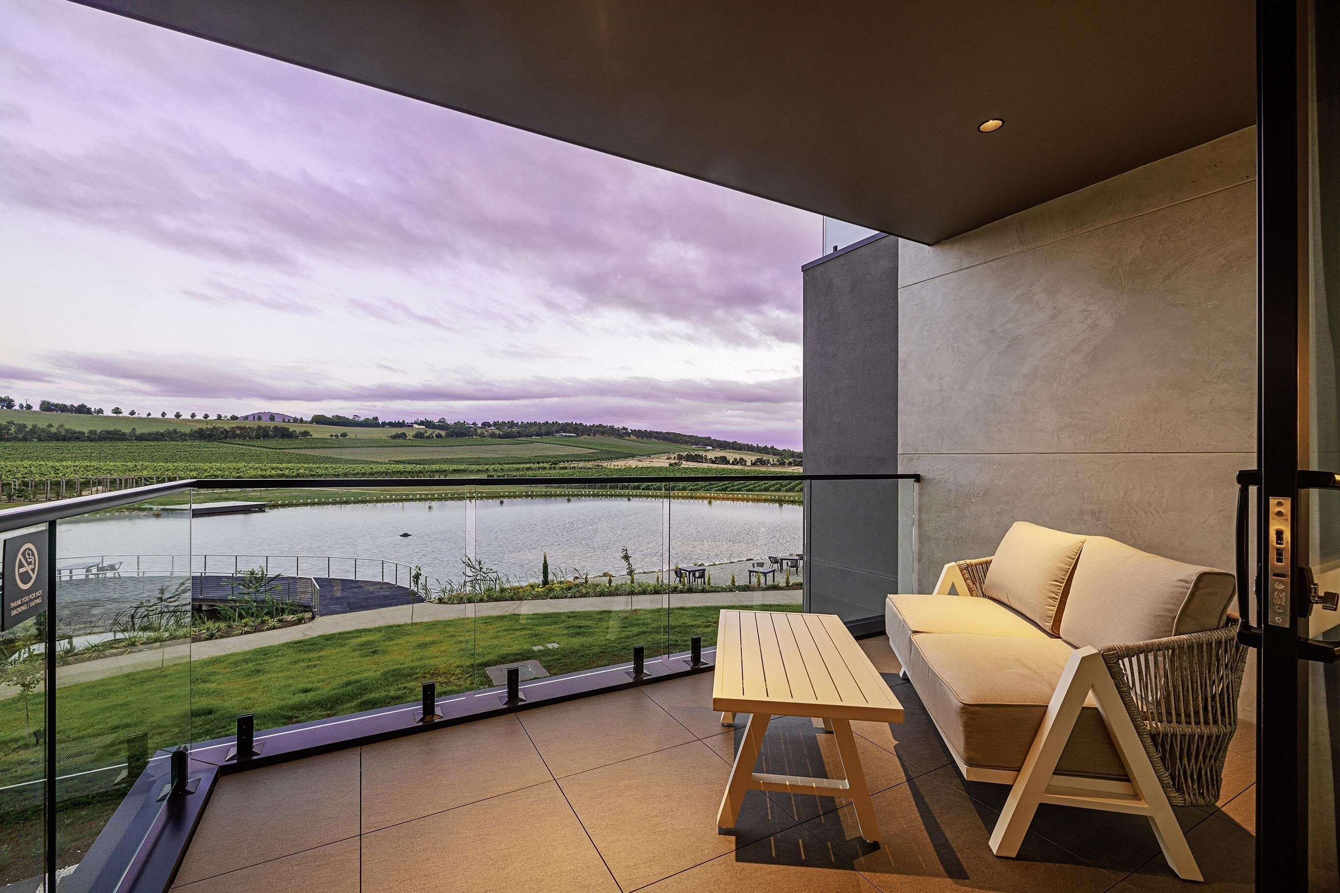 A balcony with a view of a lake, a wooden table, and a sofa.