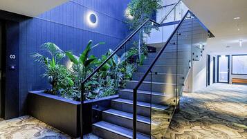 Un escalier moderne avec des rampes en verre, entouré de plantes d’intérieur, menant à un étage supérieur.