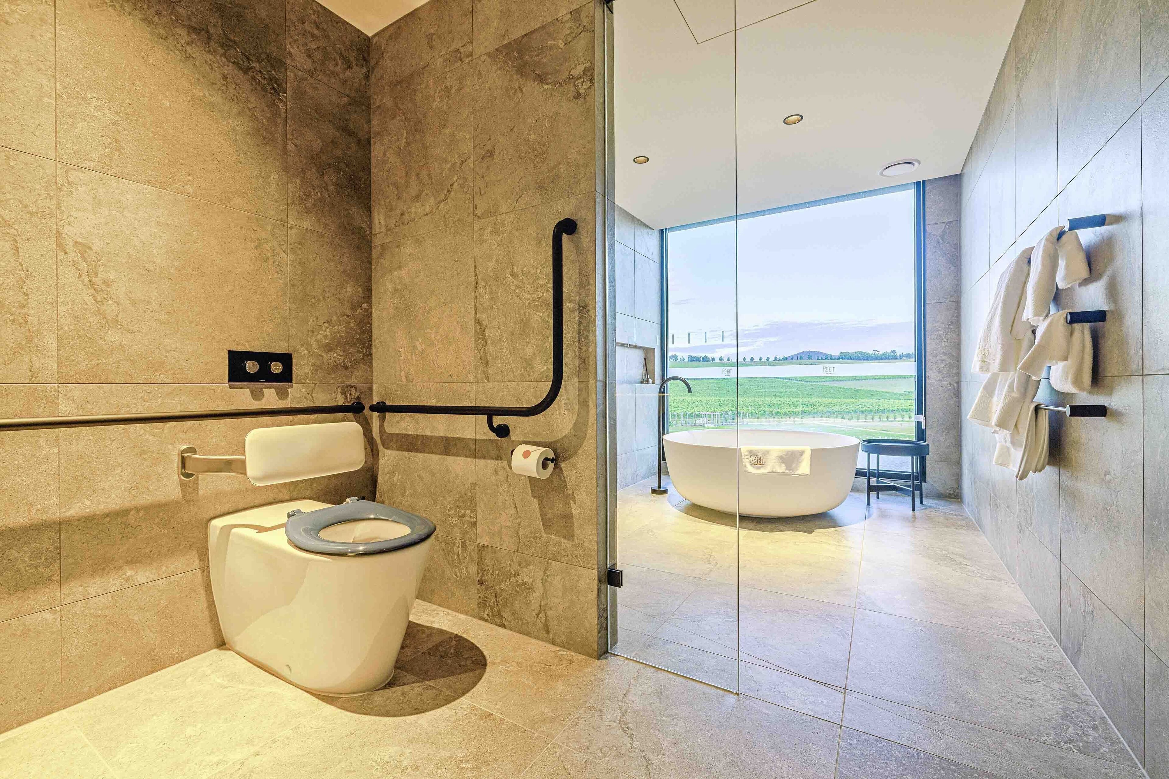 Ein modernes Badezimmer mit Toilette, Bidet und Badewanne, mit einem großen Fenster und Blick auf eine grüne Landschaft.