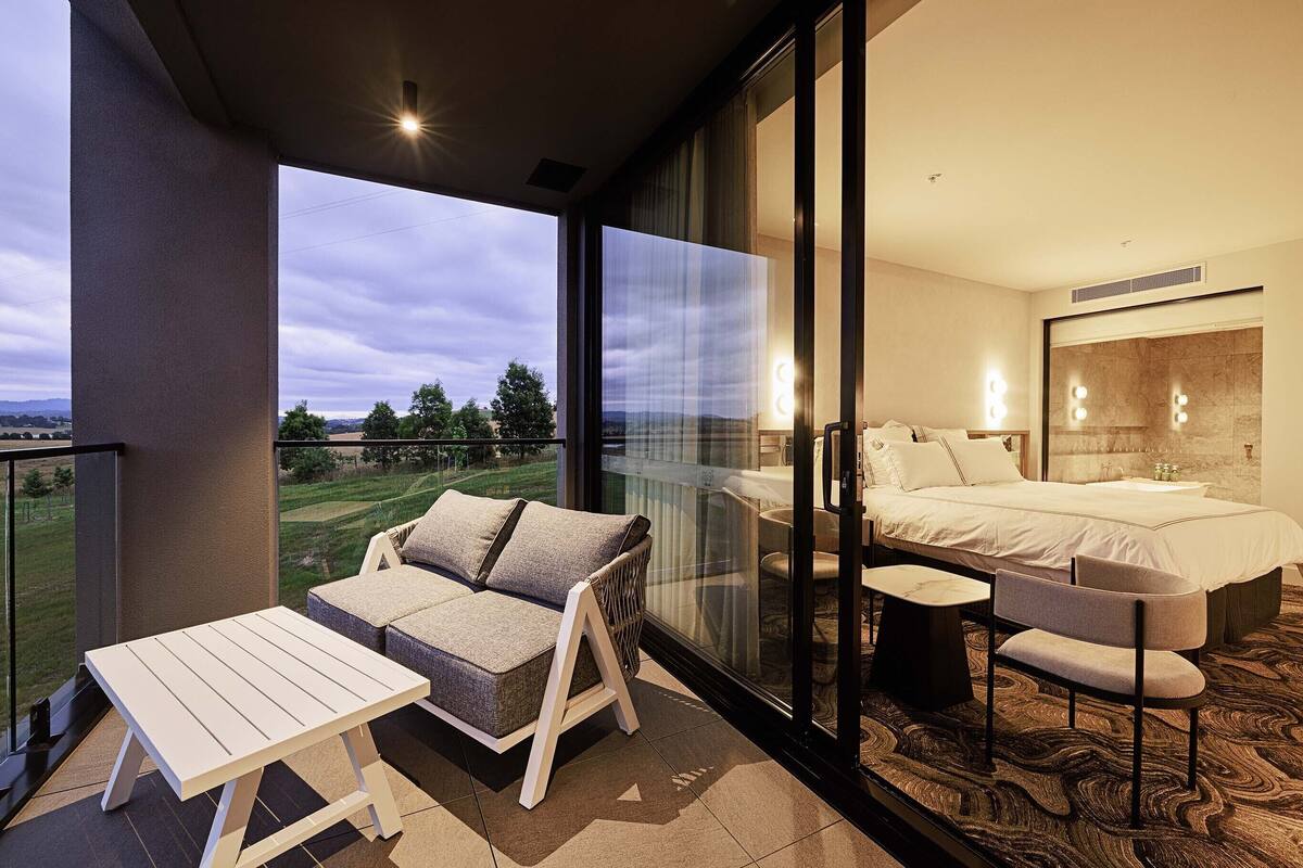 Una habitación de hotel moderna con balcón, una cama, un sofá y una silla.