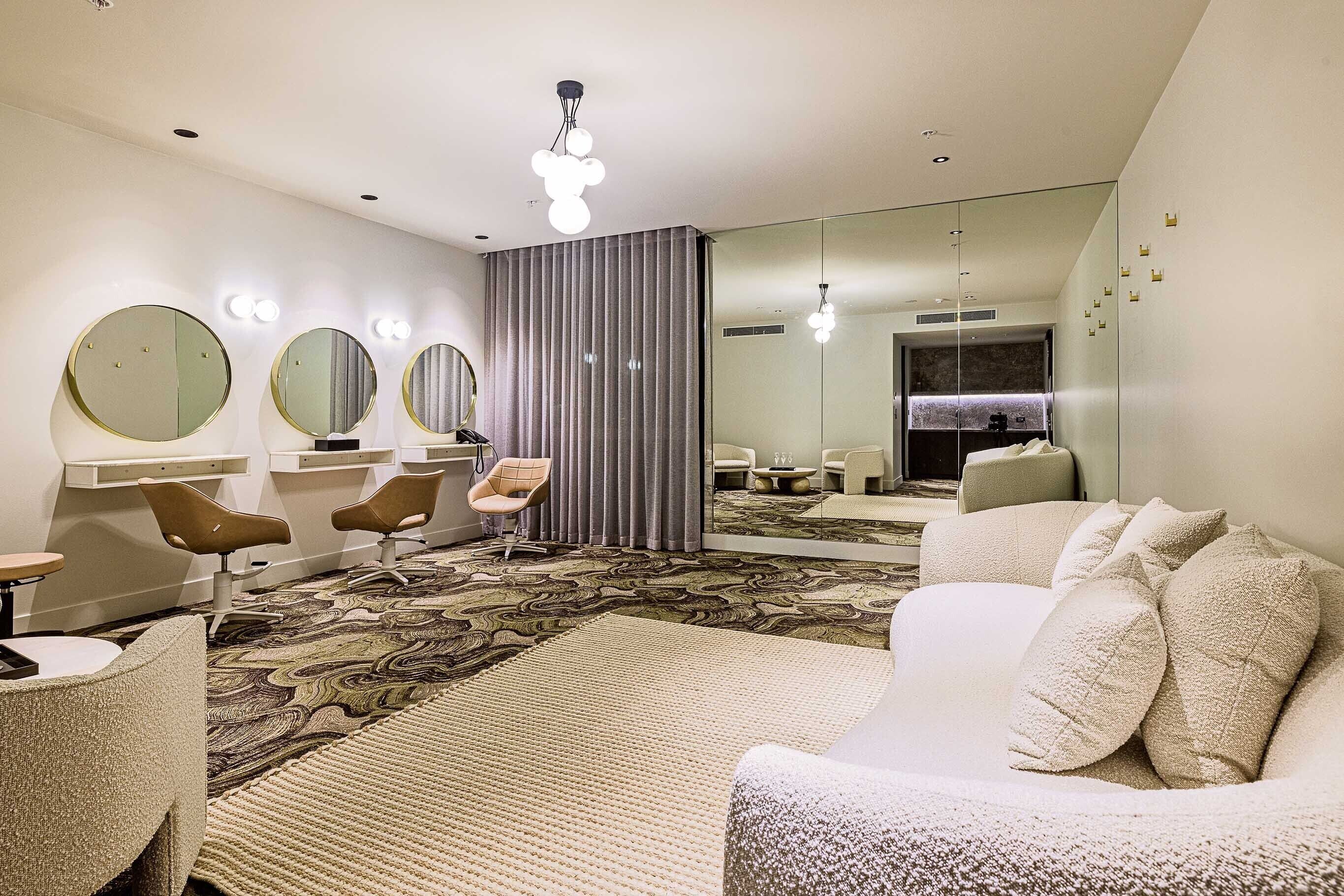 A modern hotel room with a large mirror, a sofa, a chair, and a patterned carpet.