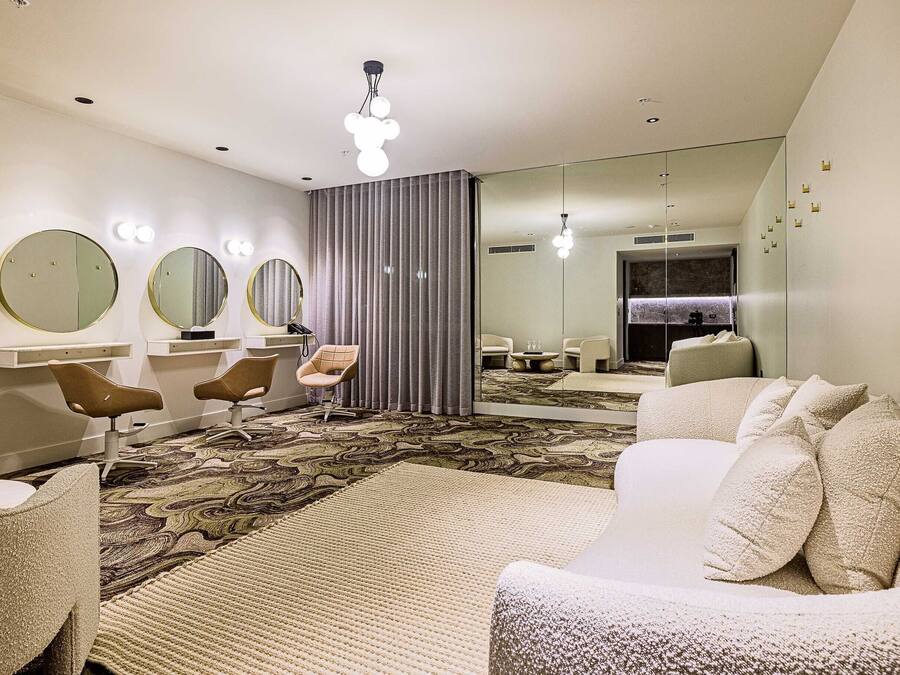 Une chambre d’hôtel moderne, dotée d’un grand miroir, d’un canapé, d’un fauteuil et d’un tapis à motifs.