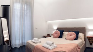 A neatly made bed with pillows, a bedside table with a lamp, and a wall-mounted light fixture. - Luxury modern apartment (Roma)