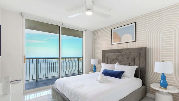A bedroom with a large bed, a ceiling fan, a view of the sea through a sliding door, and a framed picture on the wall. - Brickell Bay View Oasis with Pool, Hot Tub, & Gym (Miami)