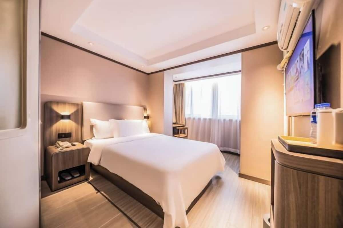 A hotel room with a large bed, bedside tables, a TV, and a window with curtains.