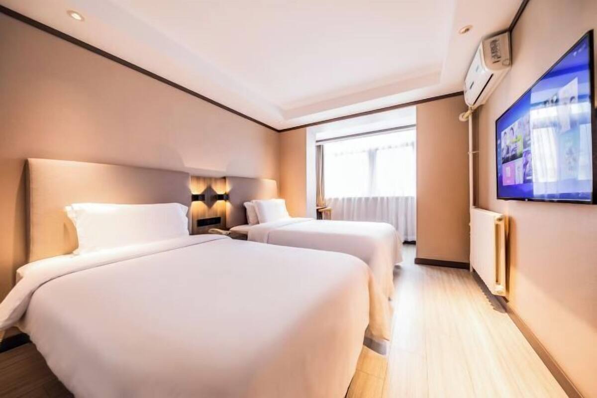 A hotel room with two beds, a TV, a window, and a wall-mounted air conditioner.