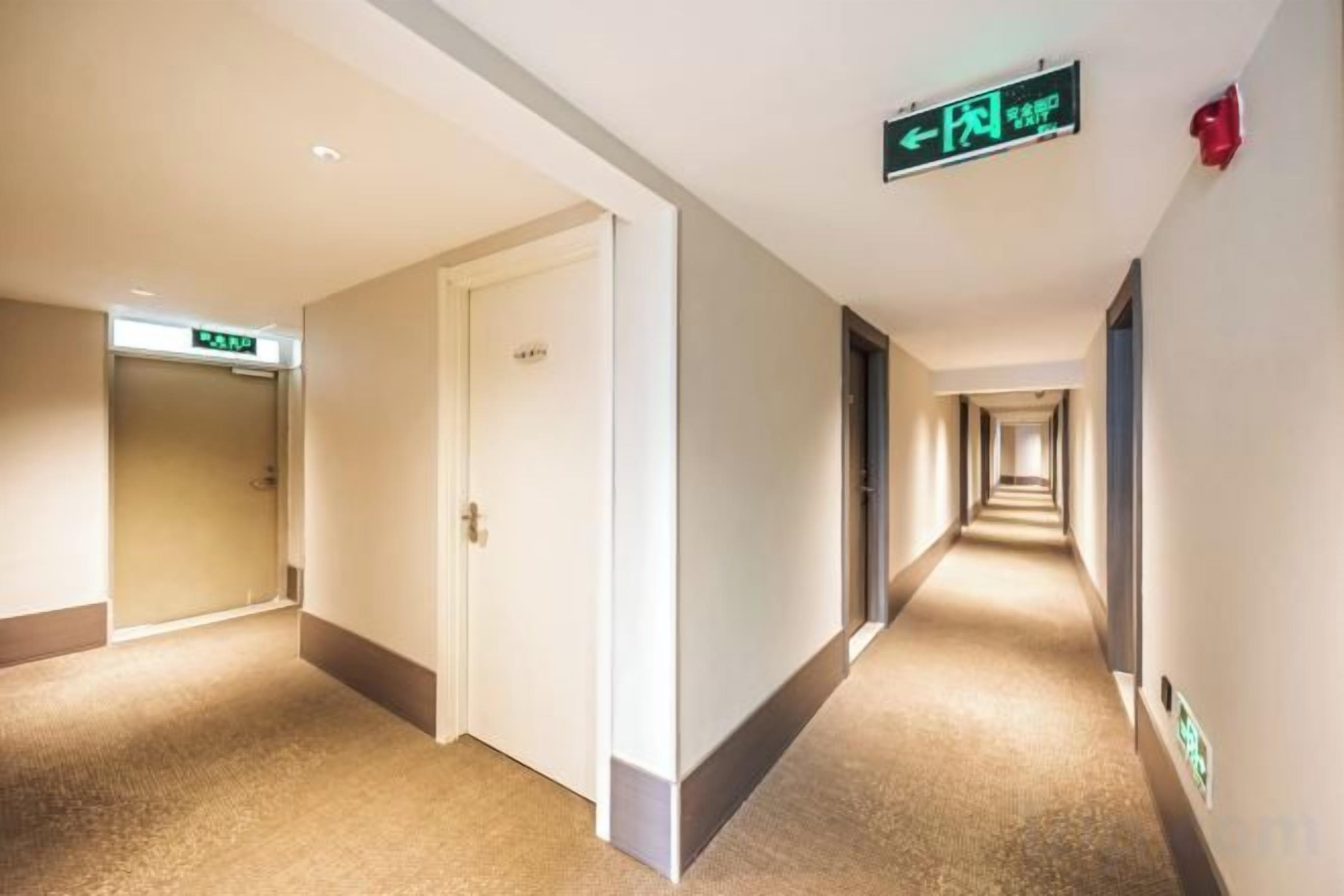 A hotel corridor with doors on both sides, an exit sign, and a fire alarm on the wall.