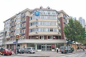 Ein mehrstöckiges Hotel mit auffälliger Beschilderung, einem Eingangsbereich im Erdgeschoss und einem sichtbaren Parkplatz.