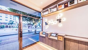 Una moderna zona de recepción con un puerta de vidrio que da a la calle, un mostrador de madera con pantalla digital y un aplique de pared.