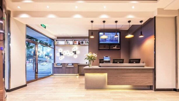 Una zona de recepción moderna con un mostrador de madera, un televisor de pantalla plana grande e iluminación colgante.