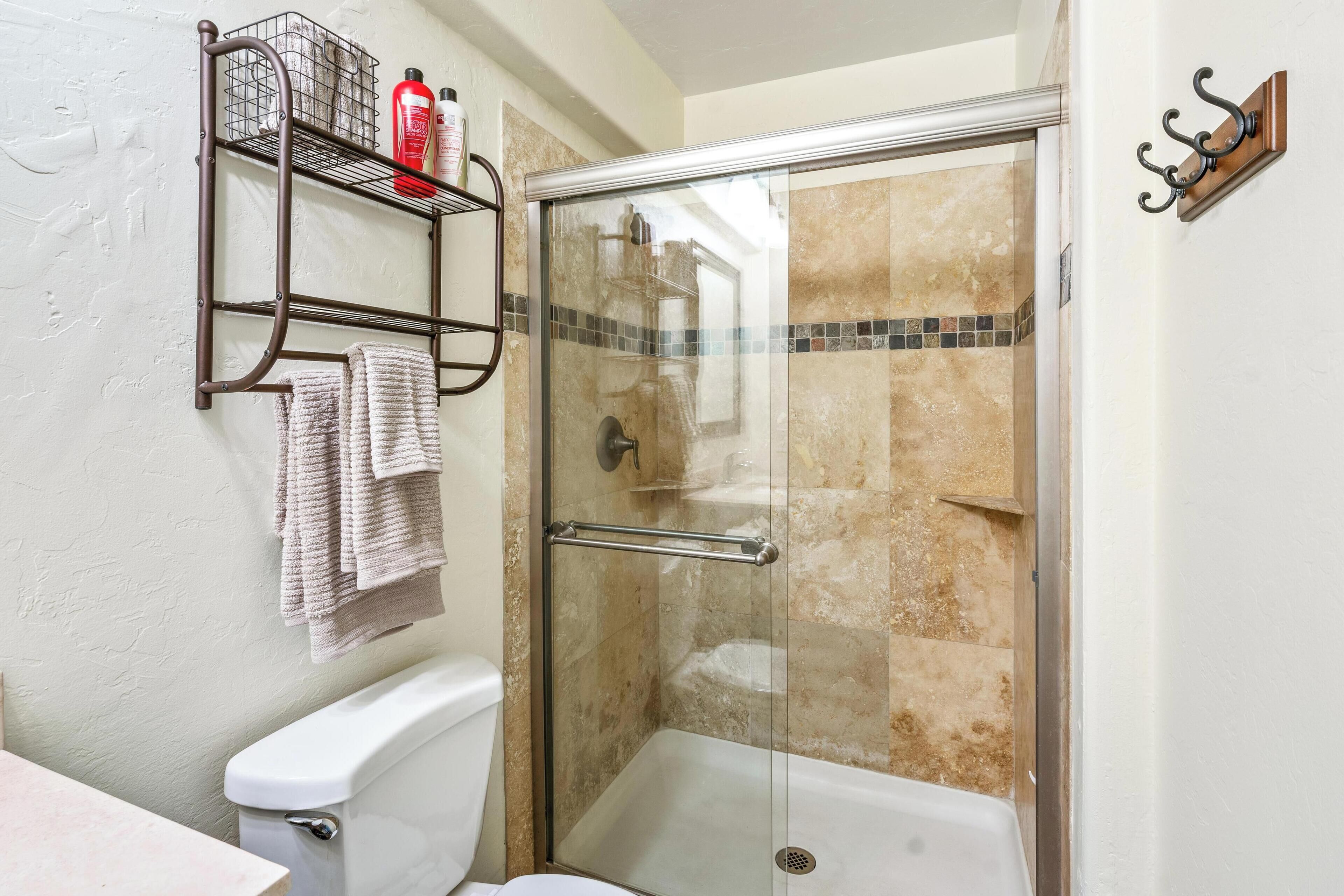 Un baño con cabina de ducha de vidrio, inodoro y toallero con toallas.