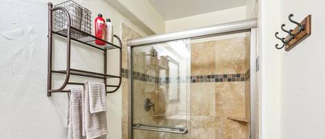 Un baño con cabina de ducha de vidrio, inodoro y toallero con toallas.