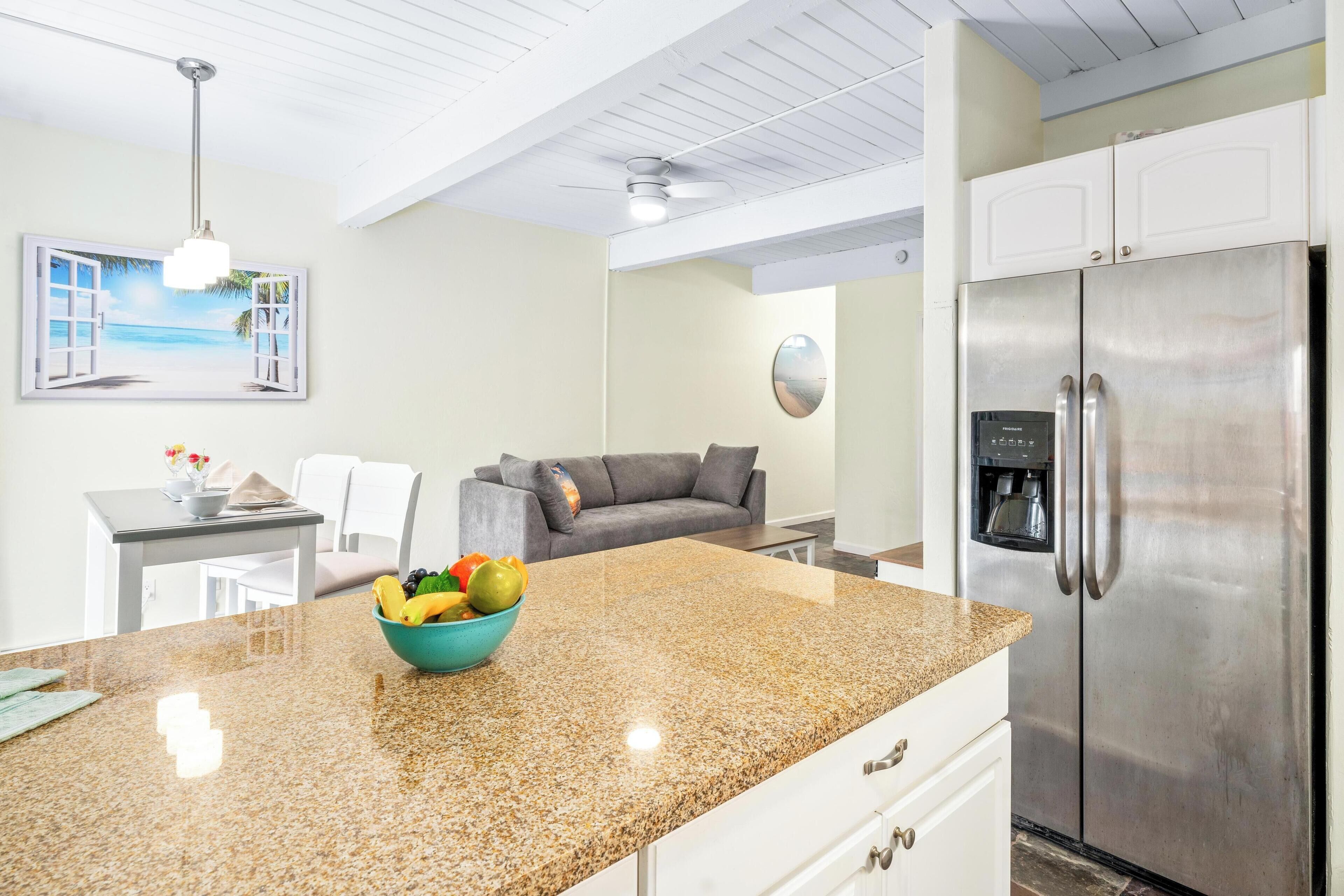 Una cocina con encimera de granito, refrigerador de acero inoxidable y comedor con mesa y sillas.