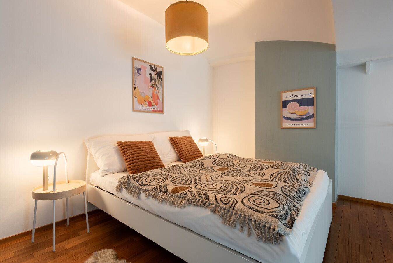 Een netjes ingerichte slaapkamer met een bed, twee bedlampen, een hanglamp en twee kunstwerken aan de muur.
