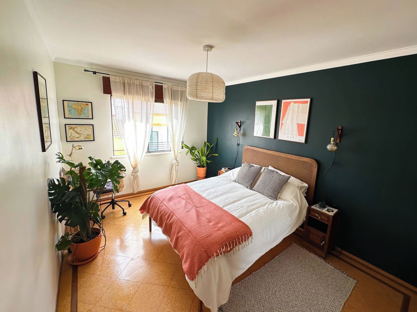 A bedroom with a bed, a desk, and two potted plants.