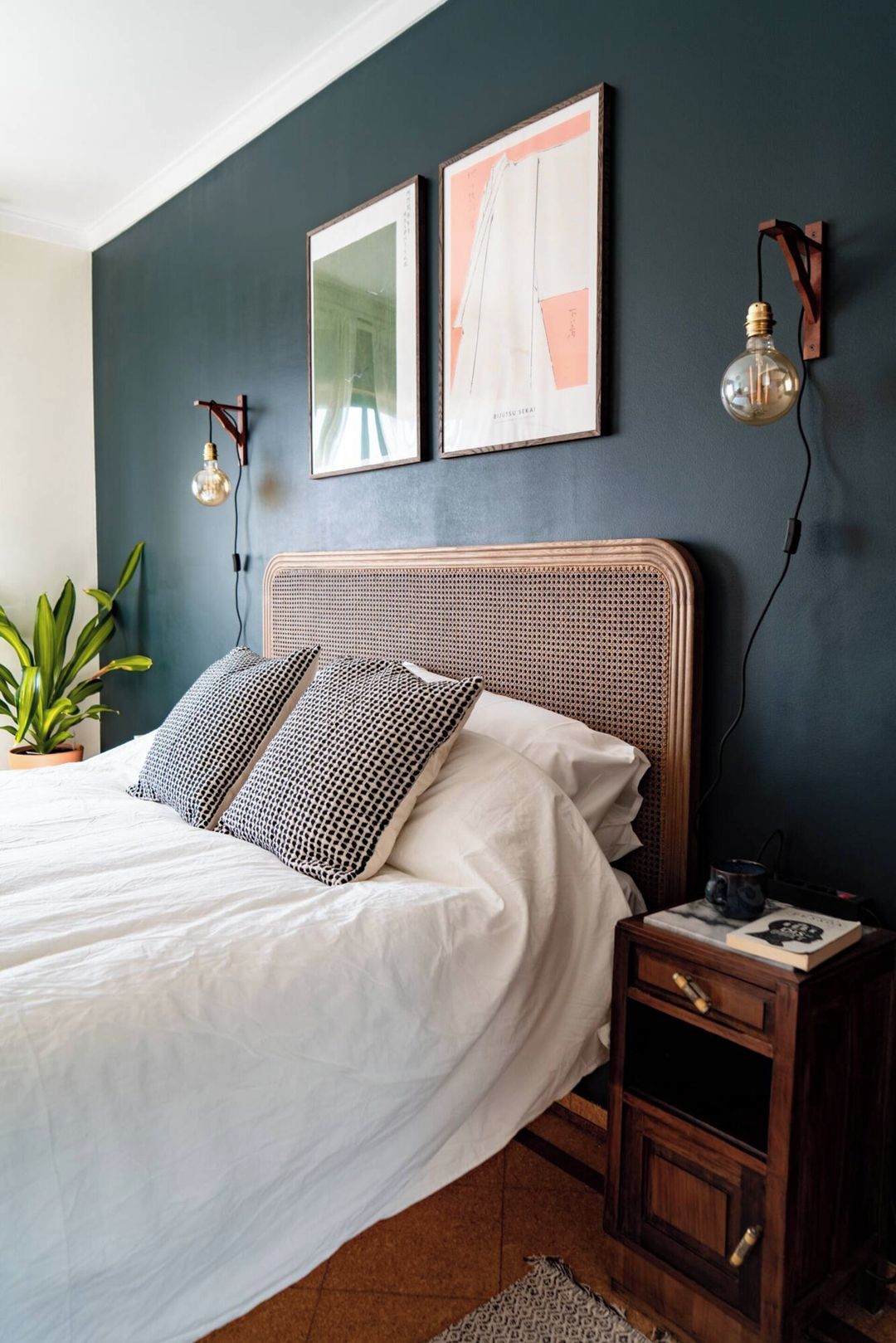 A bedroom with a bed, bedside tables, a potted plant, and wall-mounted light fixtures.