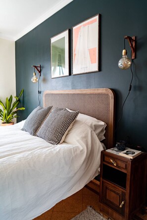 Un dormitorio con una cama, dos lámparas de pared y una mesita de noche con un libro.