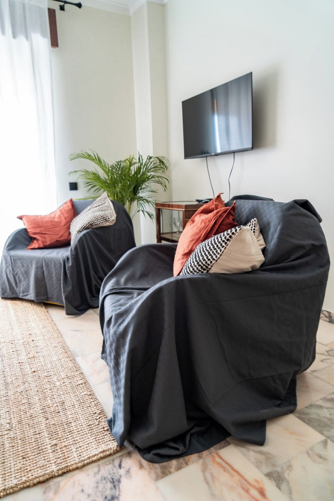 A modern living room with two black sofas, a flat-screen TV mounted on the wall, and a potted plant.