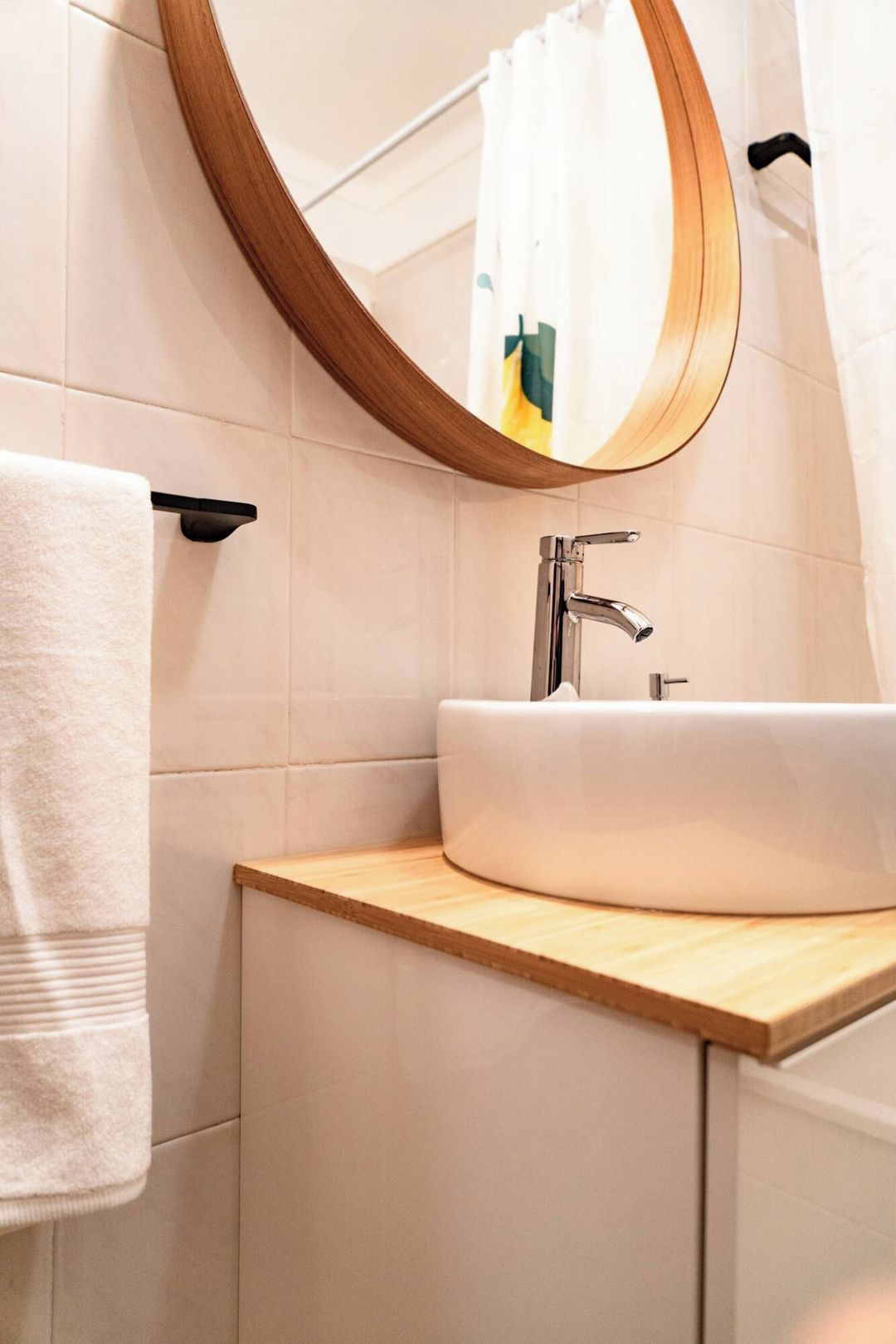 Un baño con un espejo redondo, un lavamanos blanco y un perchero para toallas.