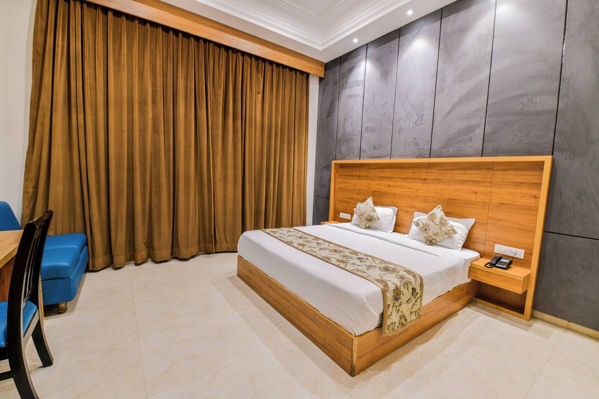 A hotel room with a wooden bed, a nightstand with a phone, a blue chair, and a large window with curtains.