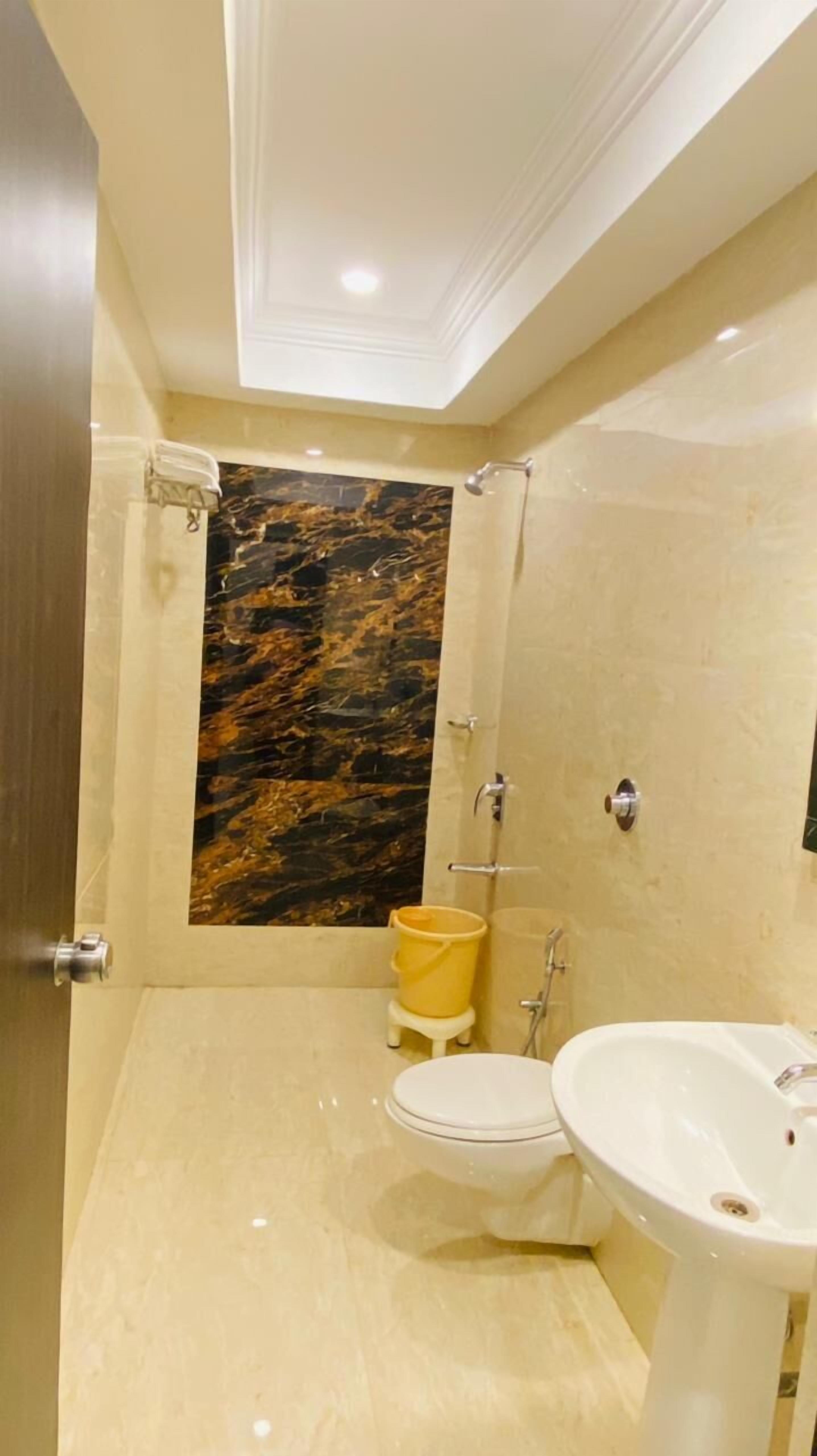 A bathroom with a marble wall, a toilet, a sink, and a shower.
